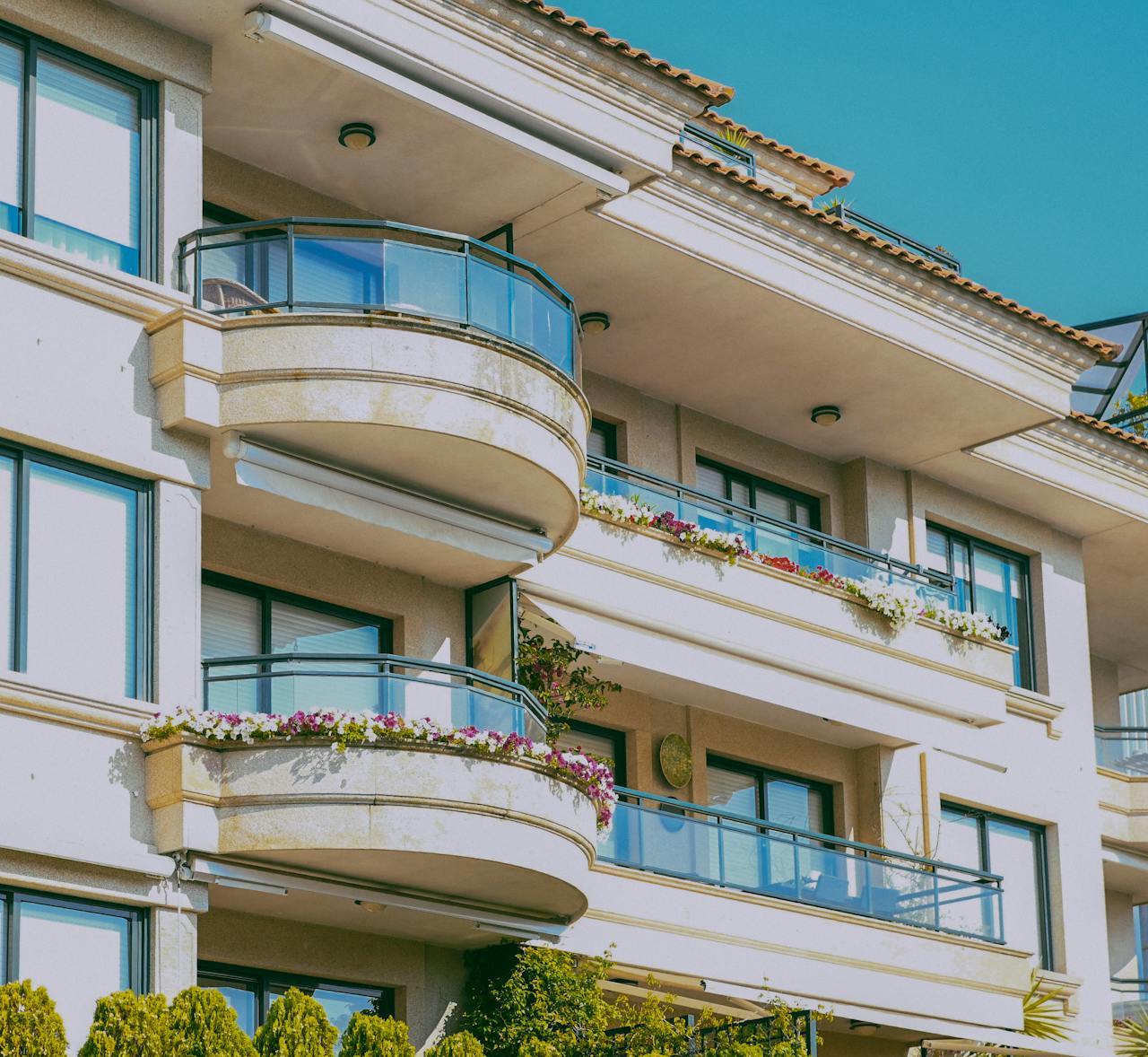 Stylish architecture featuring glass balconies and flower decorations on a sunny day.